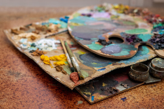 An old palette with oil paints in the artist's studio. Painted background created by a creative person. 