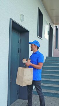 A courier knocks on the customer's door to deliver an order with ready-made food in a craft bag and coffee. home delivery of ready-made food from restaurants and cafes, courier service