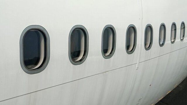 Row of aircraft cabin windows on a clean white fuselage, captured in detail with minimalistic composition and subtle reflections, symbolizing air travel and transportation