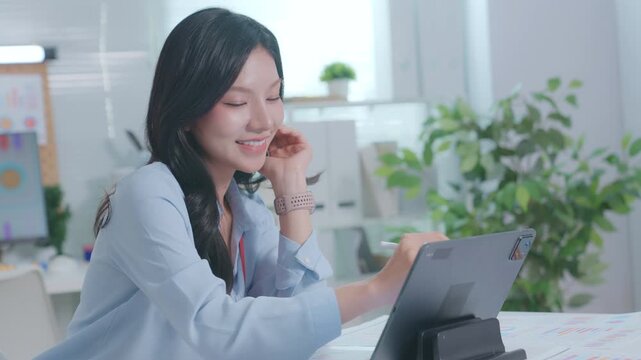 Smiling Asian Woman Working with tablet at a desk. businesswoman working from home, smiling and looking at screen. CEO businesswoman using tablet touchscreen tab device with pen
