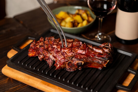 Sliced beef tagliata with tongs on cast iron grill pan with roasted potatoes and red wine