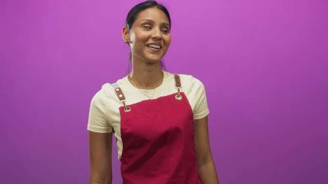 Young brunette woman in red apron smiling and turning head to side in studio; joy curiosity openness warmth.