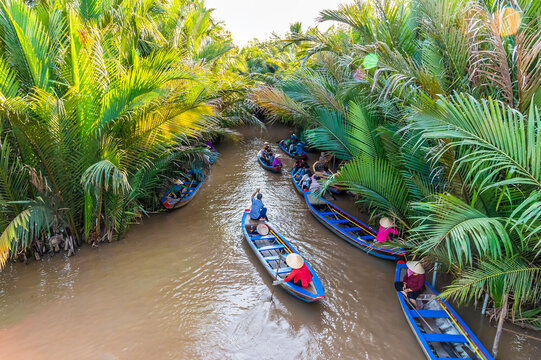 A view of traditional sampans on a coconut lined canal on coconut island on the Hau river in the Mekong Delta, Vietnam on a bright sunny day