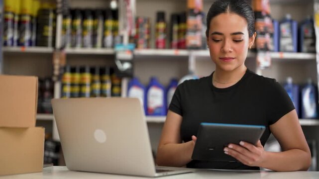 Young hispanic woman managing inventory at an auto parts store using technology