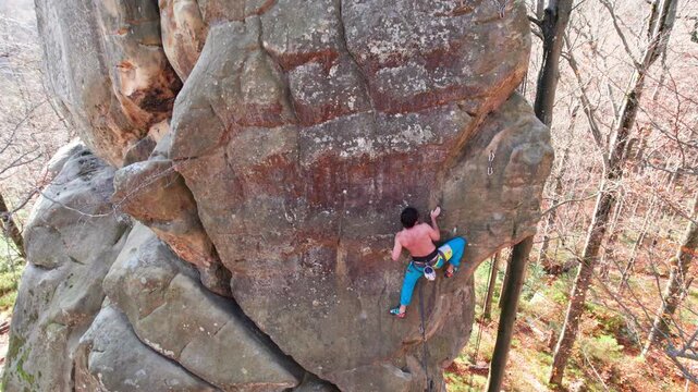 Sport climber works up vertical sandstone route with rope and quickdraws in forest. Drone footage for active recreation, training, achievement, and adrenaline driven adventure themes