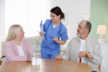Obraz premium Smiling care worker with clipboard working with senior couple at wooden table at nursing home