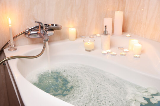 Romantic atmosphere. Bathtub with burning candles, petals and soap in bathroom, closeup