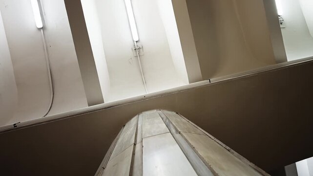 Low-angle view up a tiled escalator side and fluorescent-lit ceiling in an urban underground station, showcasing diagonal lines, industrial textures, and minimalist geometry.