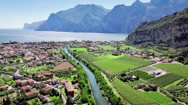 Lakeside town near Lake Garda with mountains and valley. Small European settlement with houses, fields and coastal landscape