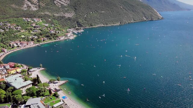 Aerial view of Lake Garda with windsurfers near lakeside Torbole town. Busy water sports area with strong wind conditions in Italy