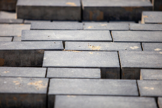 Close-up of gray rectangular concrete paving stones stacked in a stepped pattern at an outdoor construction site, with sand visible on the surface