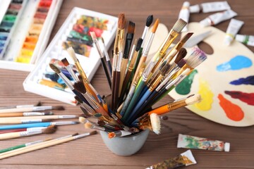 Obraz premium Paintbrushes in holder and paints on wooden table