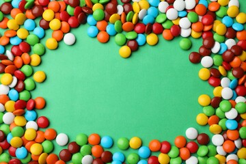 Obraz premium Delicious colorful candies on green background, flat lay. Space for text