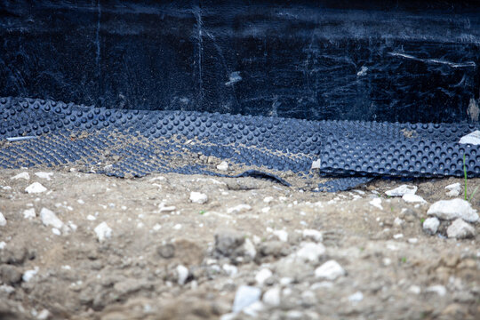 Close-up of black dimpled drainage membrane installed on a concrete foundation wall at an outdoor construction site