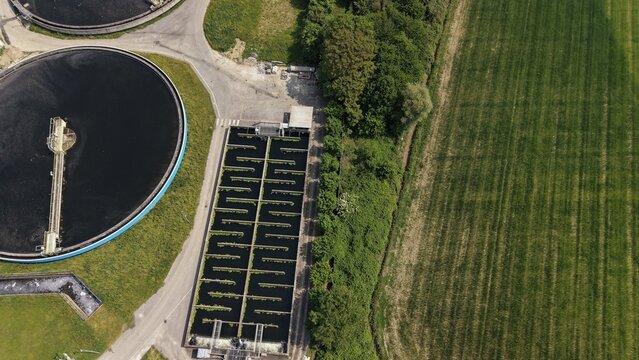 Water Treatment Plant Aerial View: An aerial perspective showcases a modern water treatment facility with circular sedimentation tanks and rectangular aeration basins, adjacent to a cultivated field.