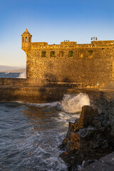 The historic stone watchtower and walls of the Batería de Santa Bárbara catch the warm evening light as waves crash against the base in Puerto de la Cruz, Tenerife © erikzunec