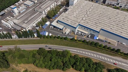 Fototapeta premium Industrial Landscape: An aerial view showcases a sprawling industrial complex with warehouses and factories, juxtaposed against a highway and lush greenery.