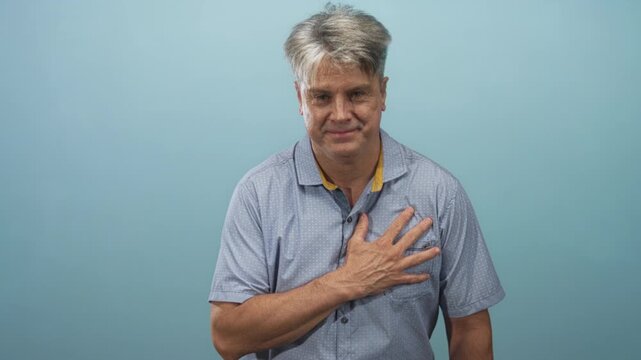 Man with grey hair places hand on chest in studio facing camera with slight smile; gratitude sincerity.