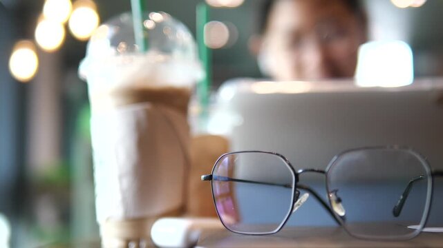 Vertical close-up of blue light blocking glasses on a digital tablet with a blurred young girl studying in the background, education and digital eye strain concept