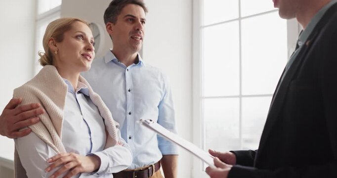 Couple and agent discuss property contract during meeting. Young clients consult a realtor in a bright apartment, reviewing terms and key options. Real estate discussion and agreement concept.