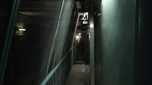 Subway tunnel corridor with narrow maintenance walkway and metal fencing, as an approaching train's headlights cut through darkness and expose urban rail infrastructure