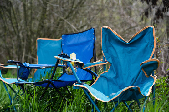 A row of blue foldable camping chairs with cup holders set up on a lush green lawn.  Evoking feelings of relaxation, picnic, or outdoor event waiting to happen.