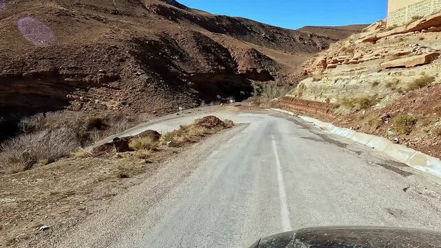 Point of view shot from a car driving on a curvy and damaged road through the desolate atlas mountains in morocco on a sunny day