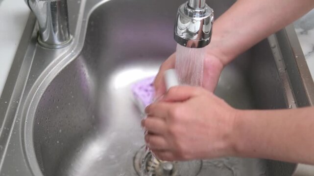Washing a white mug in the kitchen sink using a sponge and soapy water