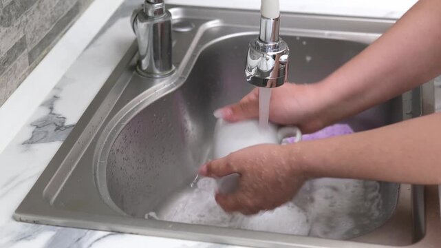 Washing a white mug in the kitchen sink using a sponge and soapy water