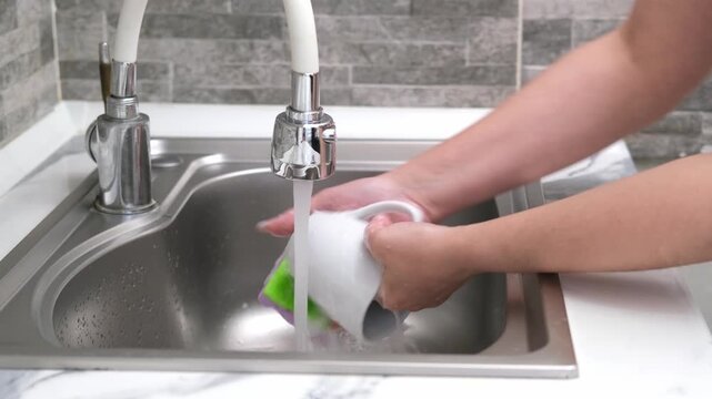 Washing a white mug in the kitchen sink using a sponge and soapy water