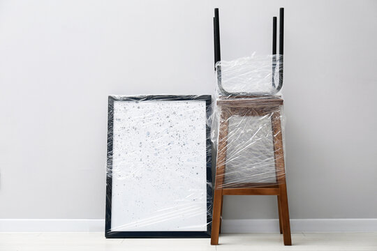 Personal belongings wrapped in plastic film for moving on floor near light grey wall
