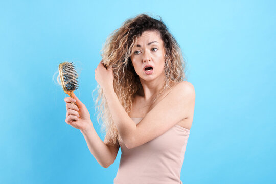 Unhappy woman trying to brush her tangled hair on light blue background