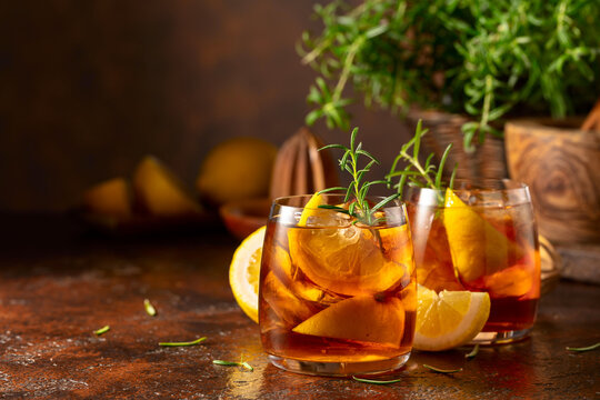 Iced tea or cocktail with ice, rosemary and lemon slices on the old brown table.