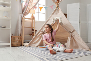Little girl playing with toys near toy wigwam in playroom, space for text © New Africa