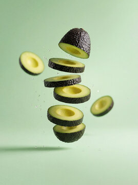 Sliced ripe avocado levitating with water droplets on light green background