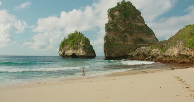 Woman running along the shoreline of Diamond Beach under massive cliffs in Nusa Penida