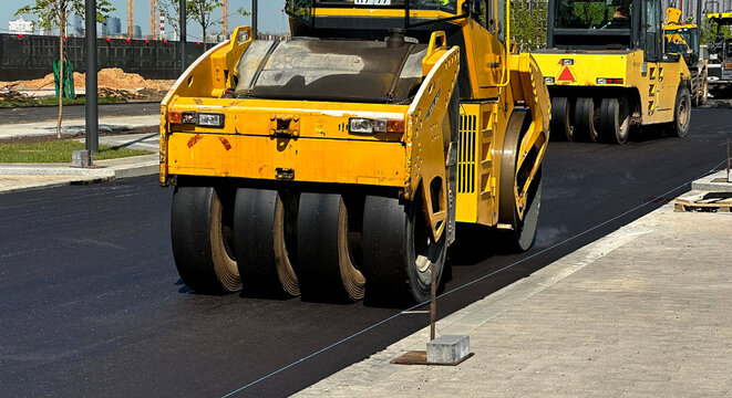 Yellow rollers compact fresh asphalt on a new road