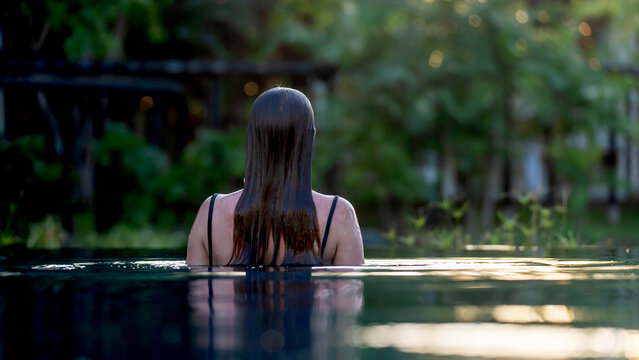 Woman stands in calm pool, back to camera