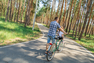 Naklejka premium Dad rides his daughter in a bicycle seat in forest. A man carries a small child on a bicycle.
