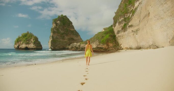 Woman walks along wide sandy shore toward the large rocks at Diamond Beach in Nusa Penida Bali