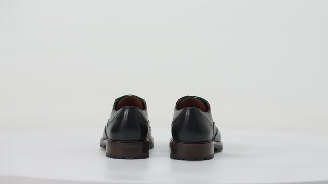 Black leather classic brogue oxford shoes with thick soles rotating on a turntable isolated on a white background