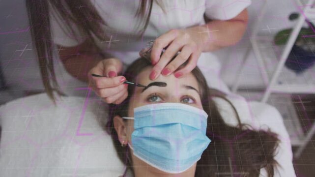 Spa tech leaning over client on bed holding forehead taut using brush applying pigment shaping brow