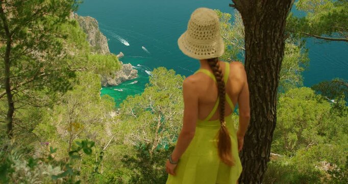 Woman walking through Capri pines overlooking vibrant turquoise Tyrrhenian Sea in summer