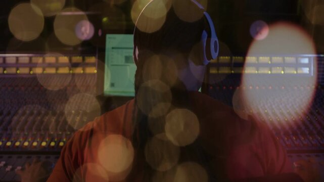 Engineer donning headset after screen glow leaning toward console adjusting faders and checking mix