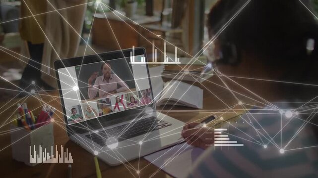Elementary girl writing in notebook at desk watching laptop with moving data overlay, copy space