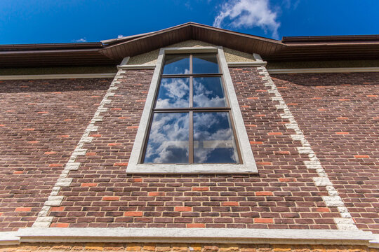 A view of a large window on a brick wall. The window shows reflections of clouds in the blue sky. This setting is in an urban area during the day