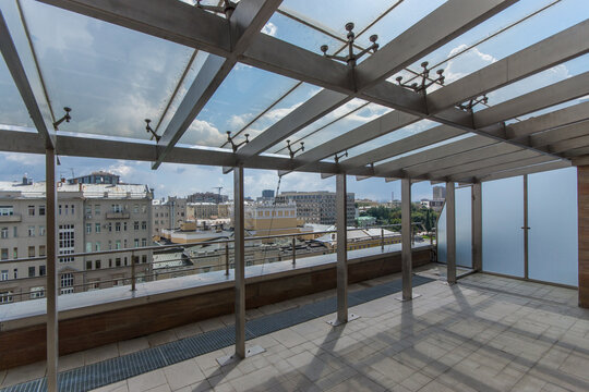 People can see a rooftop terrace with metal structures and glass panels. The terrace offers views of a busy city with buildings under a clear sky