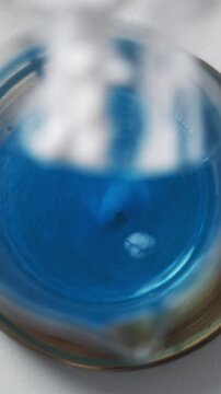 Close-up view of a chemical reaction where a solvent changes color from green to blue. The process illustrates titration or dissolution