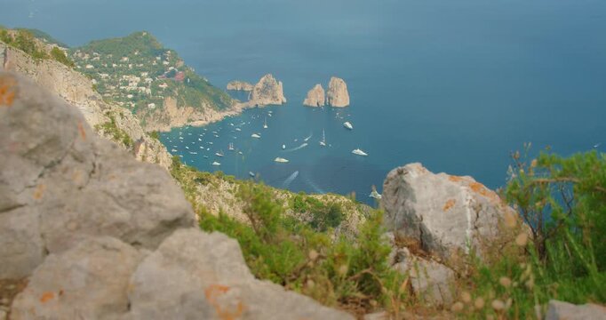 Capri town and Faraglioni sea stacks viewed from rocky ridge on calm bright summer day
