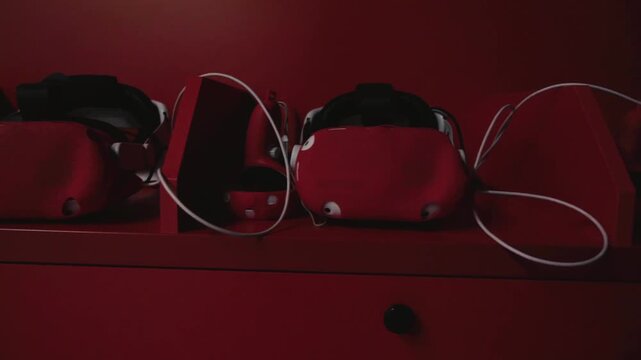 Red VR headset rests on a matching surface. Wires connect to the device, indicating active use. No people are visible, so emotions are not applicable. Ideal for tech, gaming